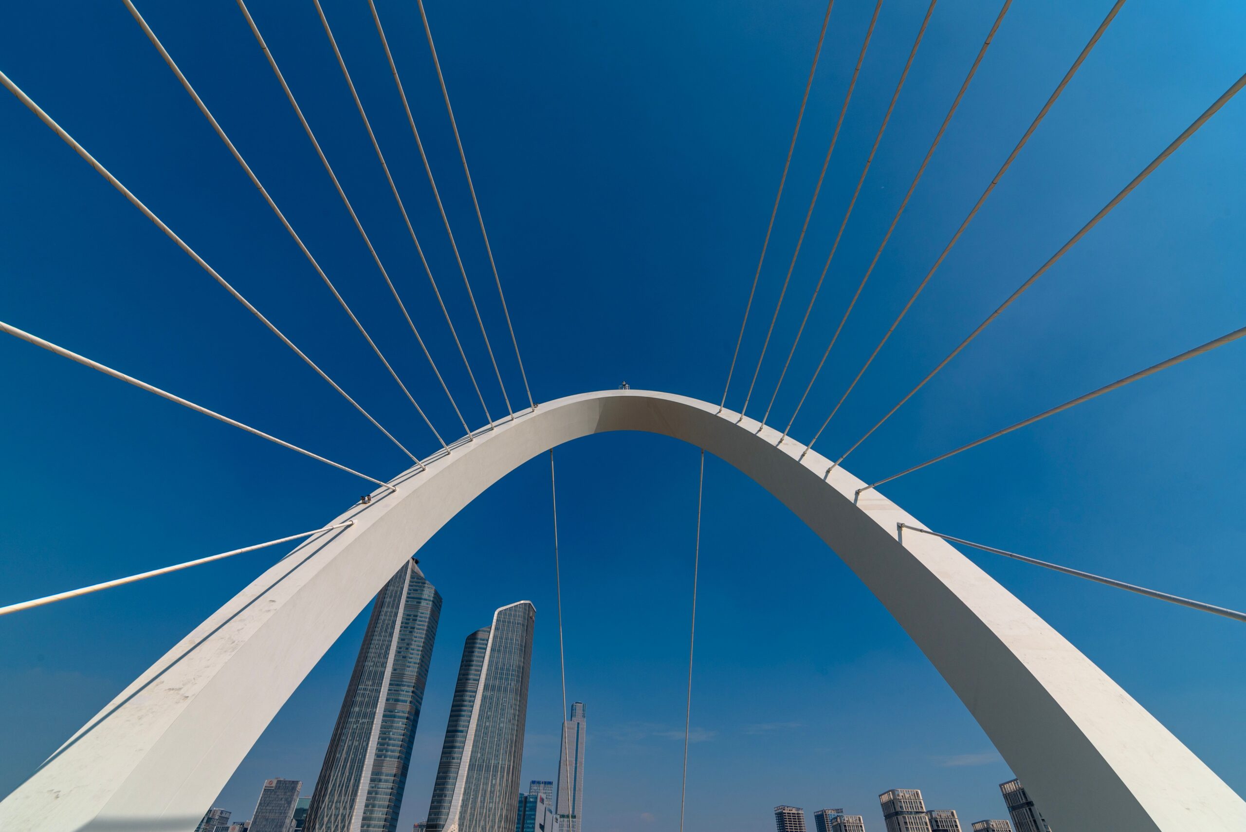 Dramatic view of a modern suspension bridge and skyscrapers in Nanjing against a blue sky.